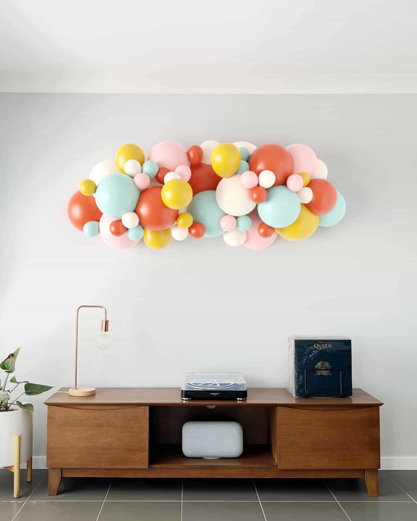 A vibrant balloon garland in pastel and bold colors, adorning a minimalist wall above a wooden console table.