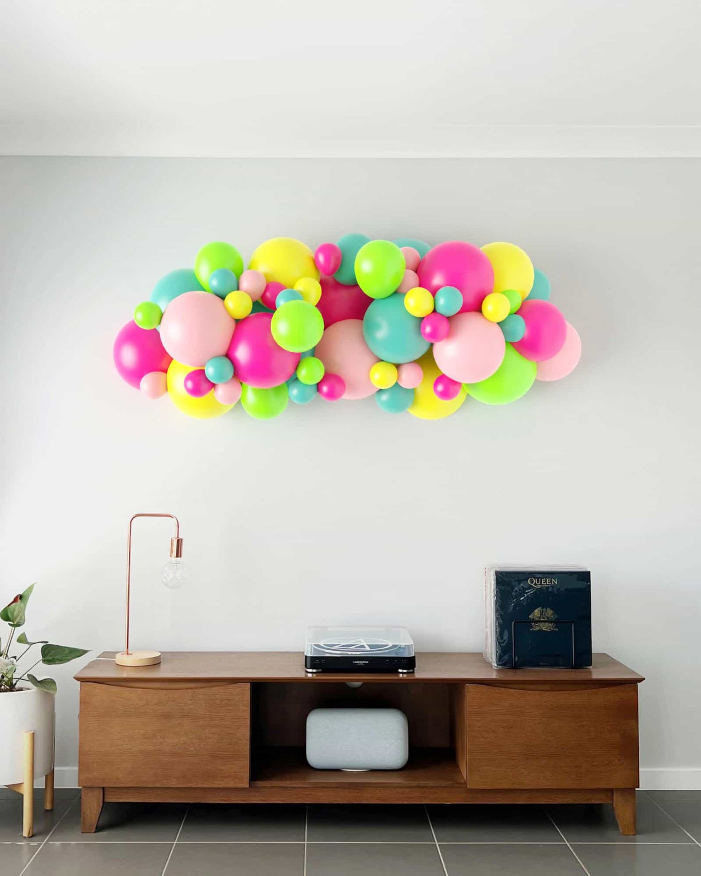 Colorful balloon garland in pink, green, yellow, and blue, mounted on a light wall above a wooden table.