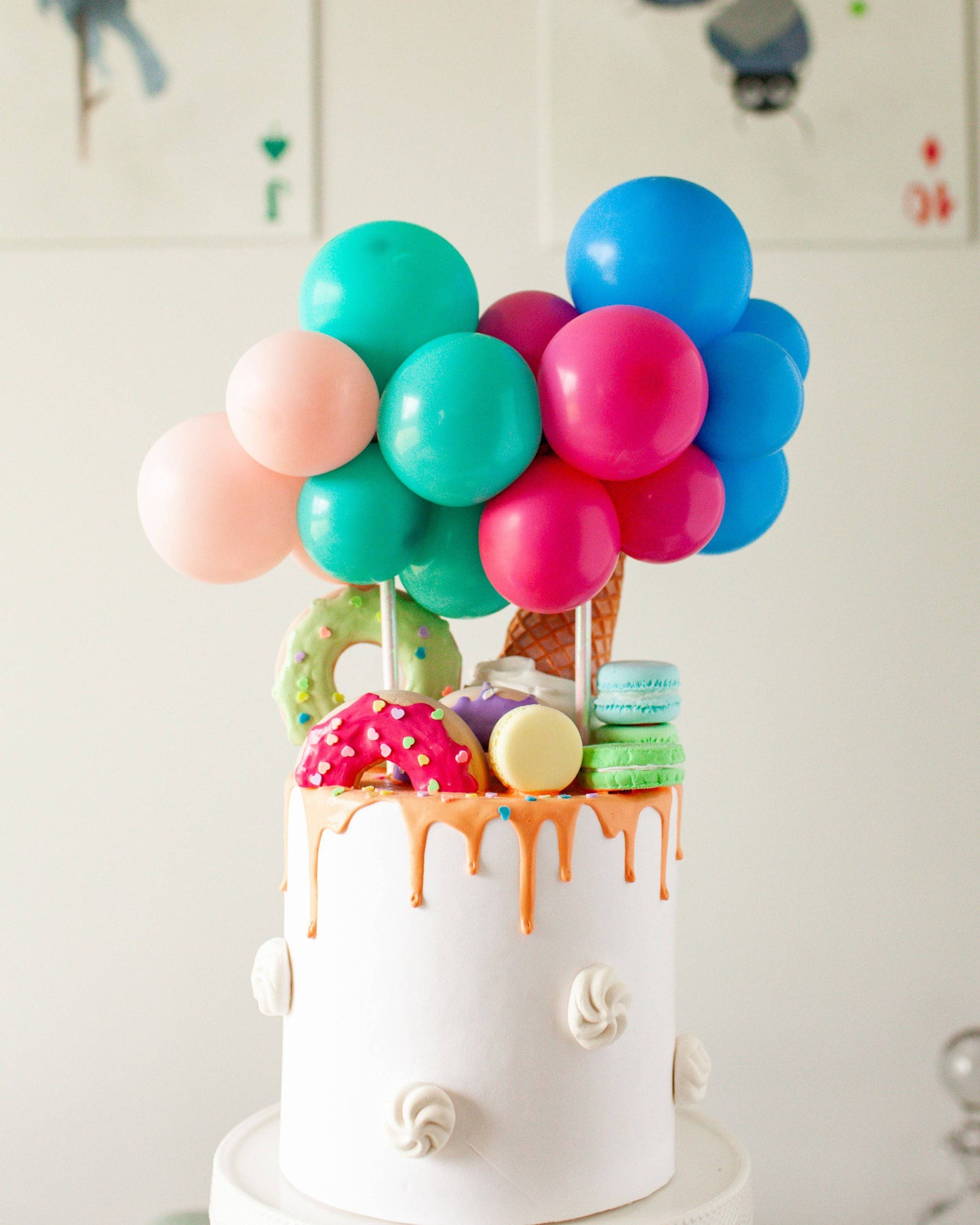 A colorful cake topped with balloons, sprinkles, donuts, ice cream cones, and macarons creates a festive vibe.