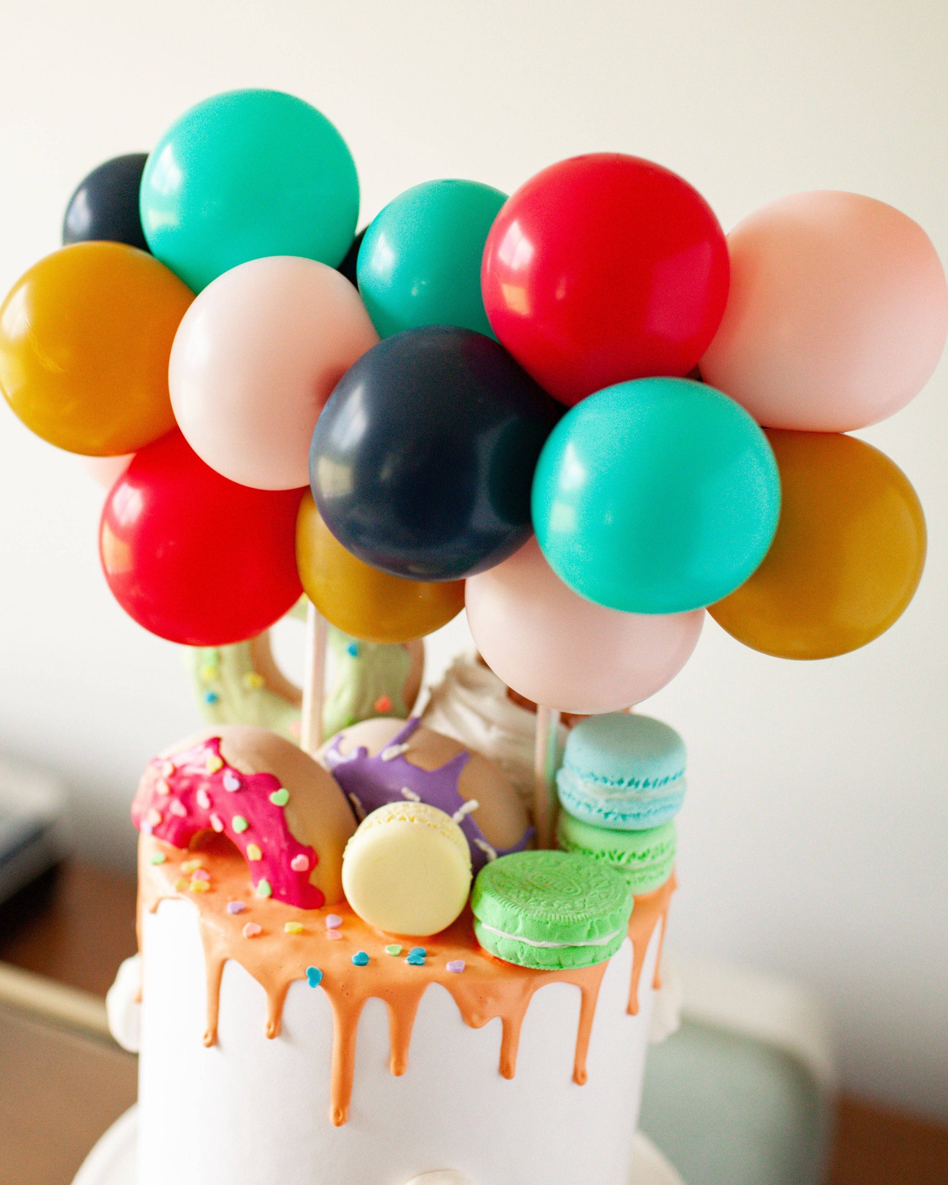 Colorful balloons in various sizes top a tiered confection, surrounded by playful, vibrant decorations.