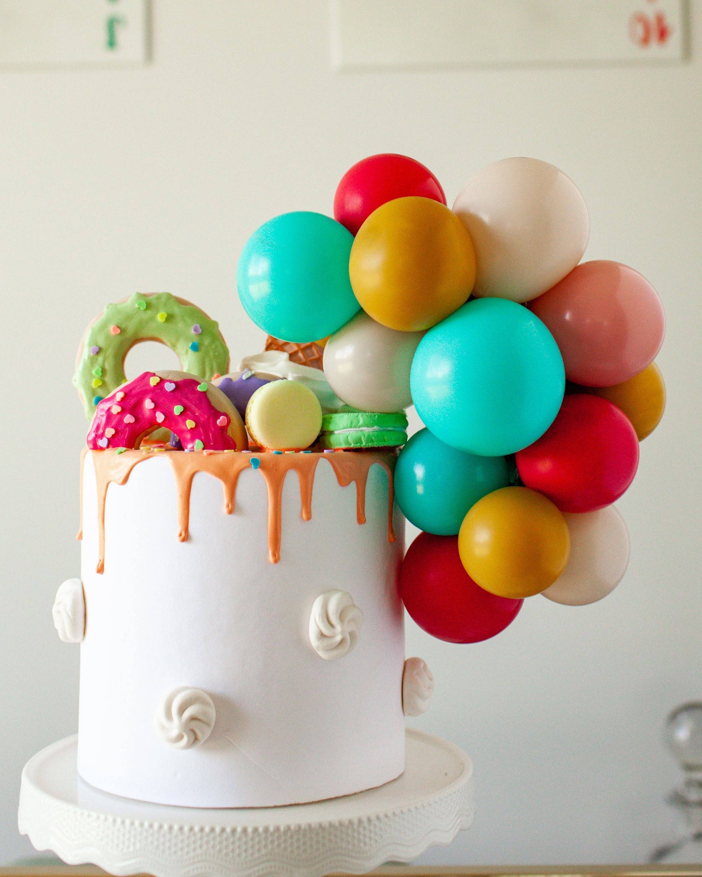 Colorful balloons and sweet treats adorn a white cake with dripping icing, creating a festive and vibrant display.