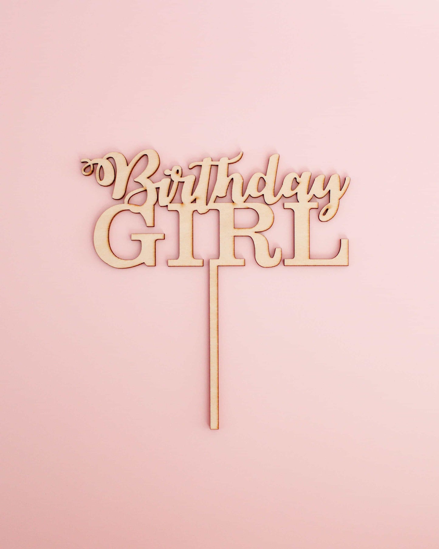 Wooden cake topper featuring the phrase "Birthday Girl" in an elegant font against a soft pink background.