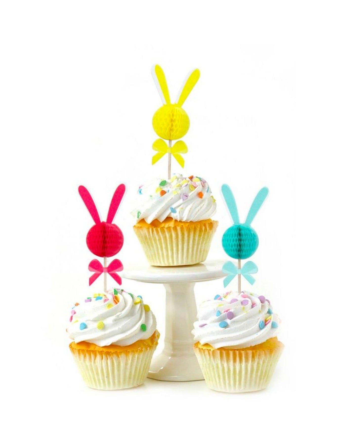 Colorful bunny-shaped picks atop frosted cupcakes with sprinkles on a white pedestal stand.