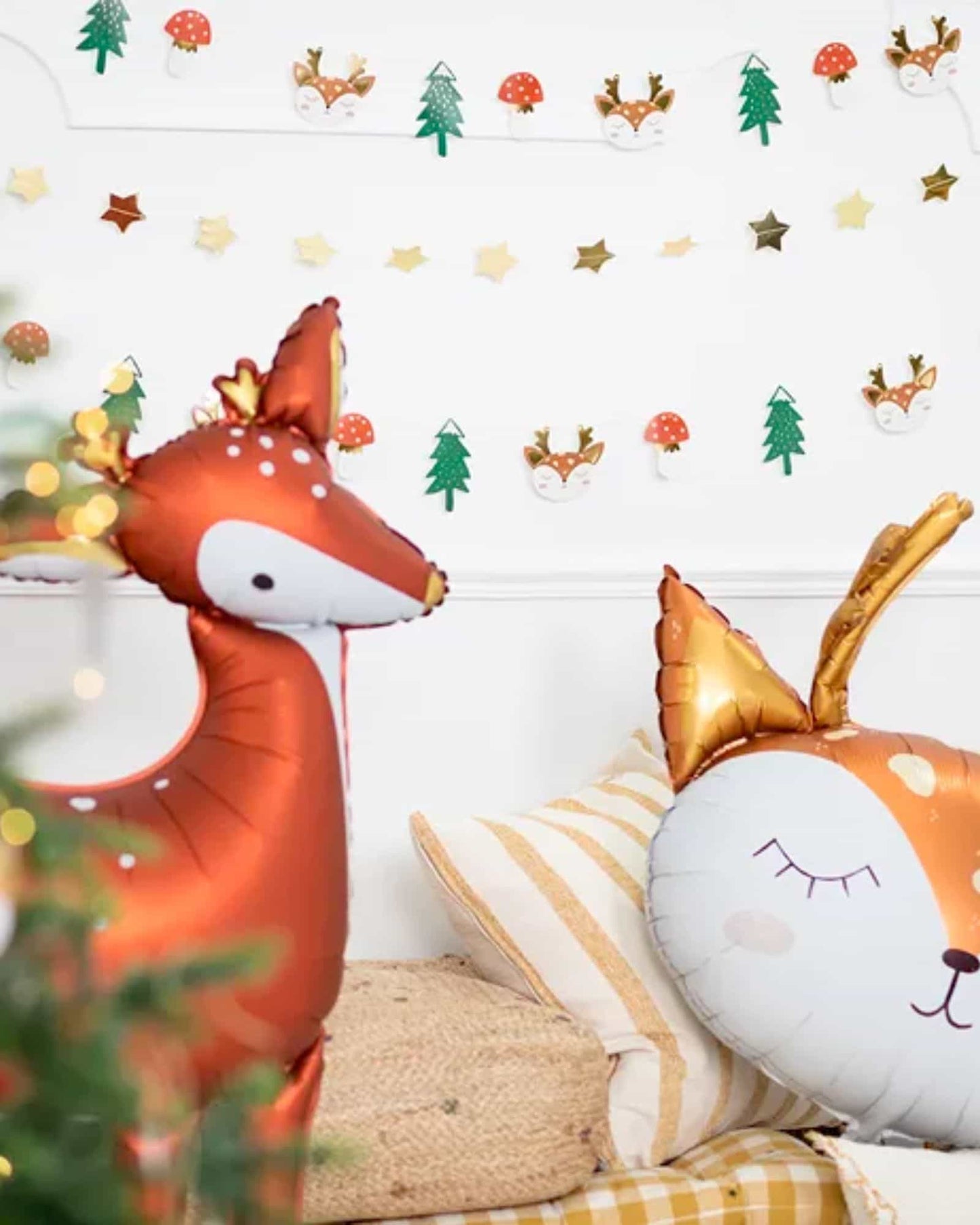A shiny, orange deer balloon stands beside a cute, sleeping face pillow in a festive, decorated room.