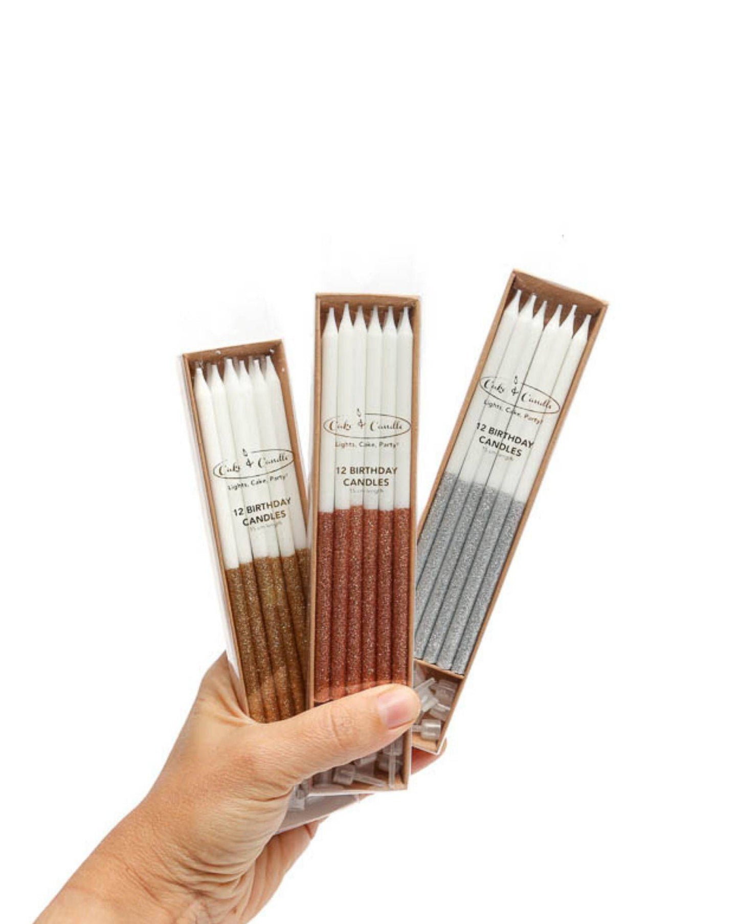 Three packs of glitter-dipped tall candles in gold, copper, and silver, held in a hand against a white background.