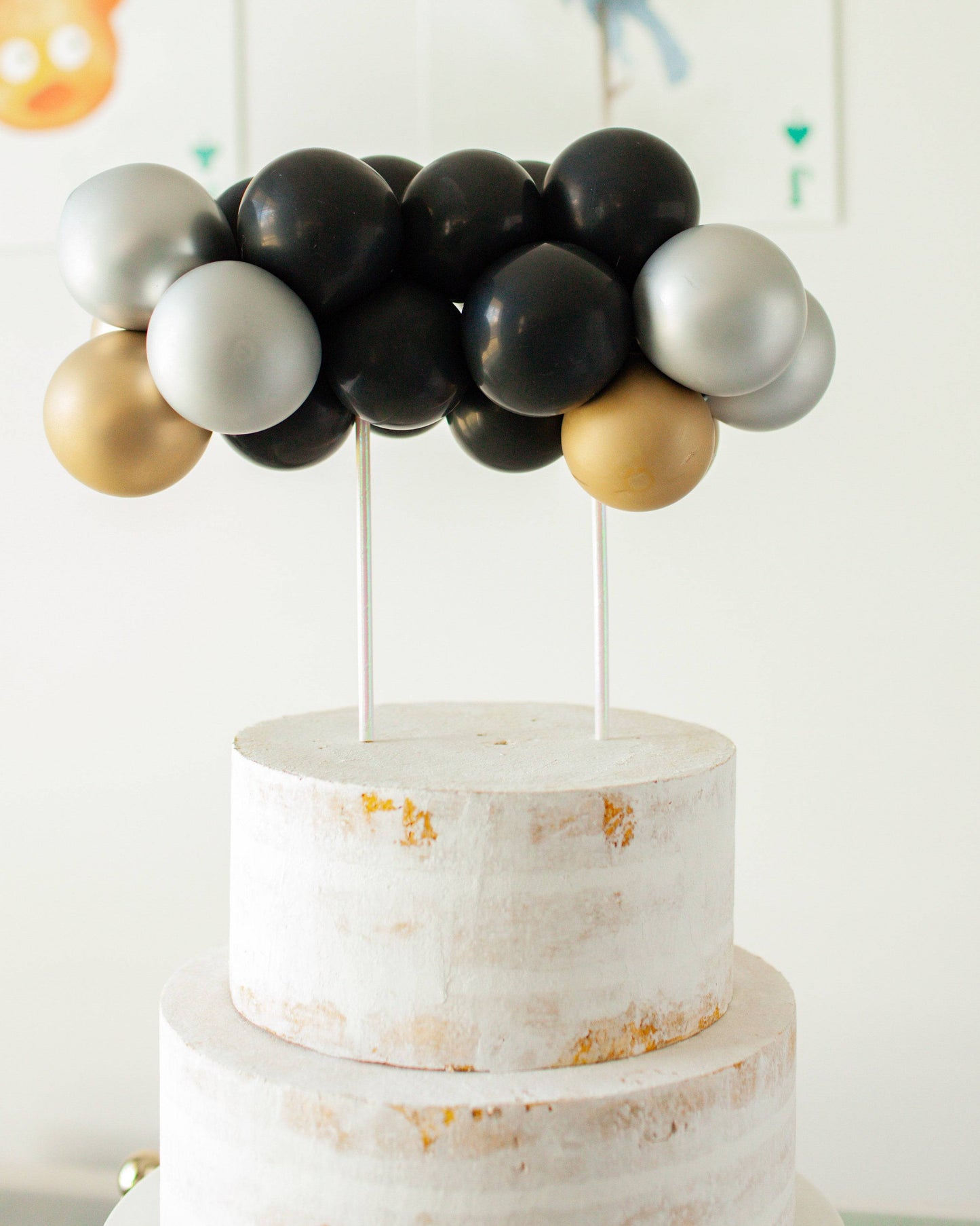A cluster of black, silver, and gold balloons atop a white, textured, tiered structure.