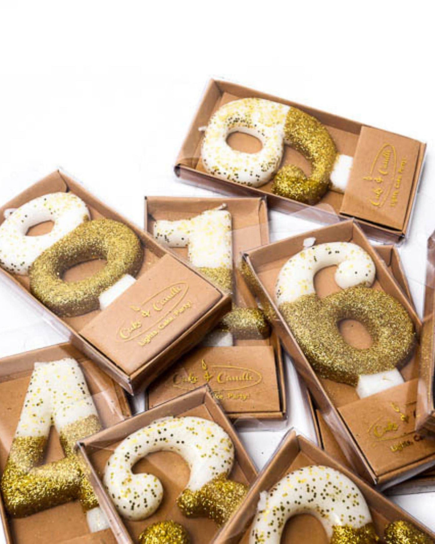 Gold glitter-dipped candle in the shape of the number 8, nestled in a clear box with other decorative candles.