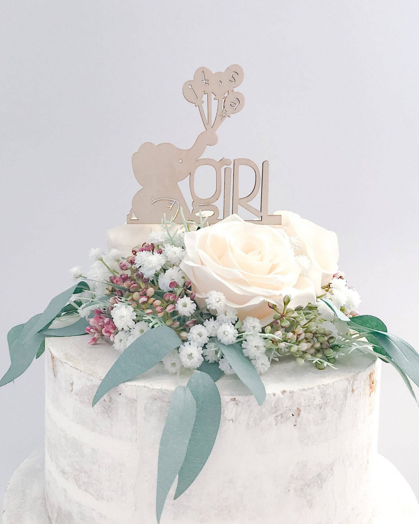 A sweet wooden topper featuring an elephant holding balloons, surrounded by delicate flowers and greenery.