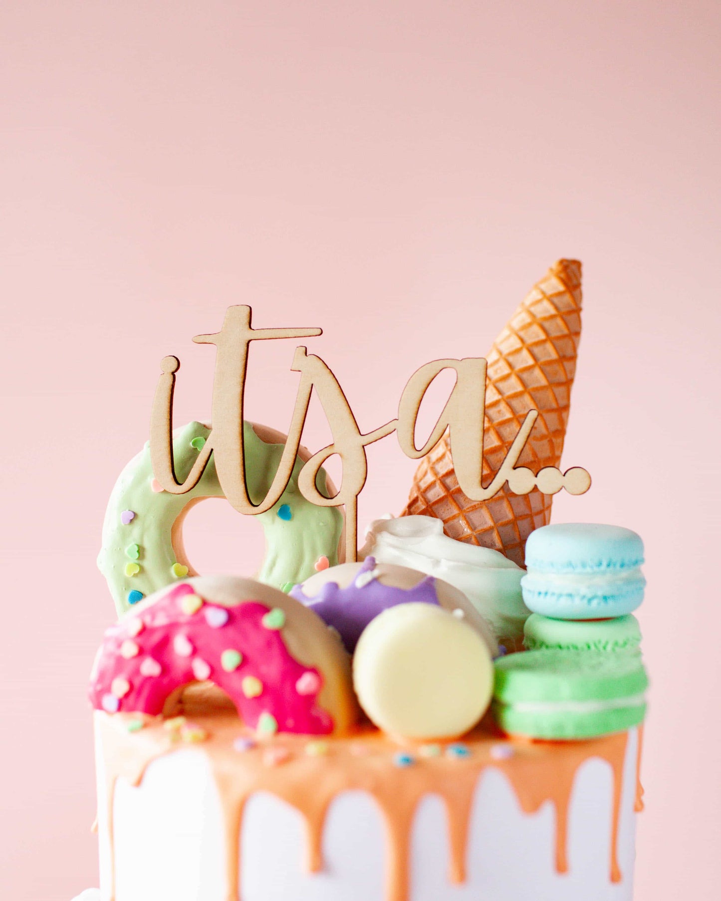 Wooden topper reads "it’s a..." atop a colorful arrangement of treats including donuts and ice cream cones.