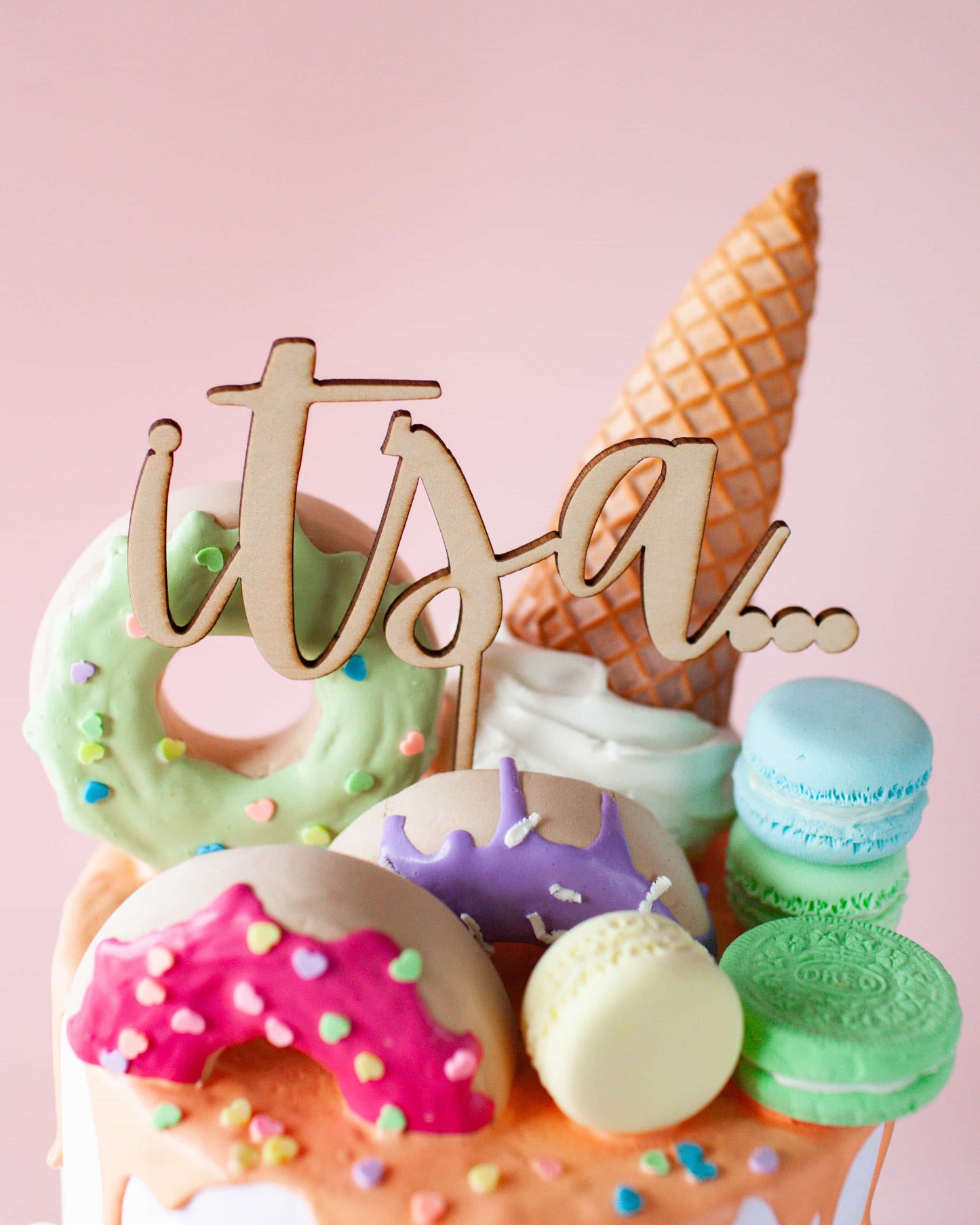A wooden topper with "itsa..." above vibrant, colorful desserts including donuts, macarons, and an ice cream cone.