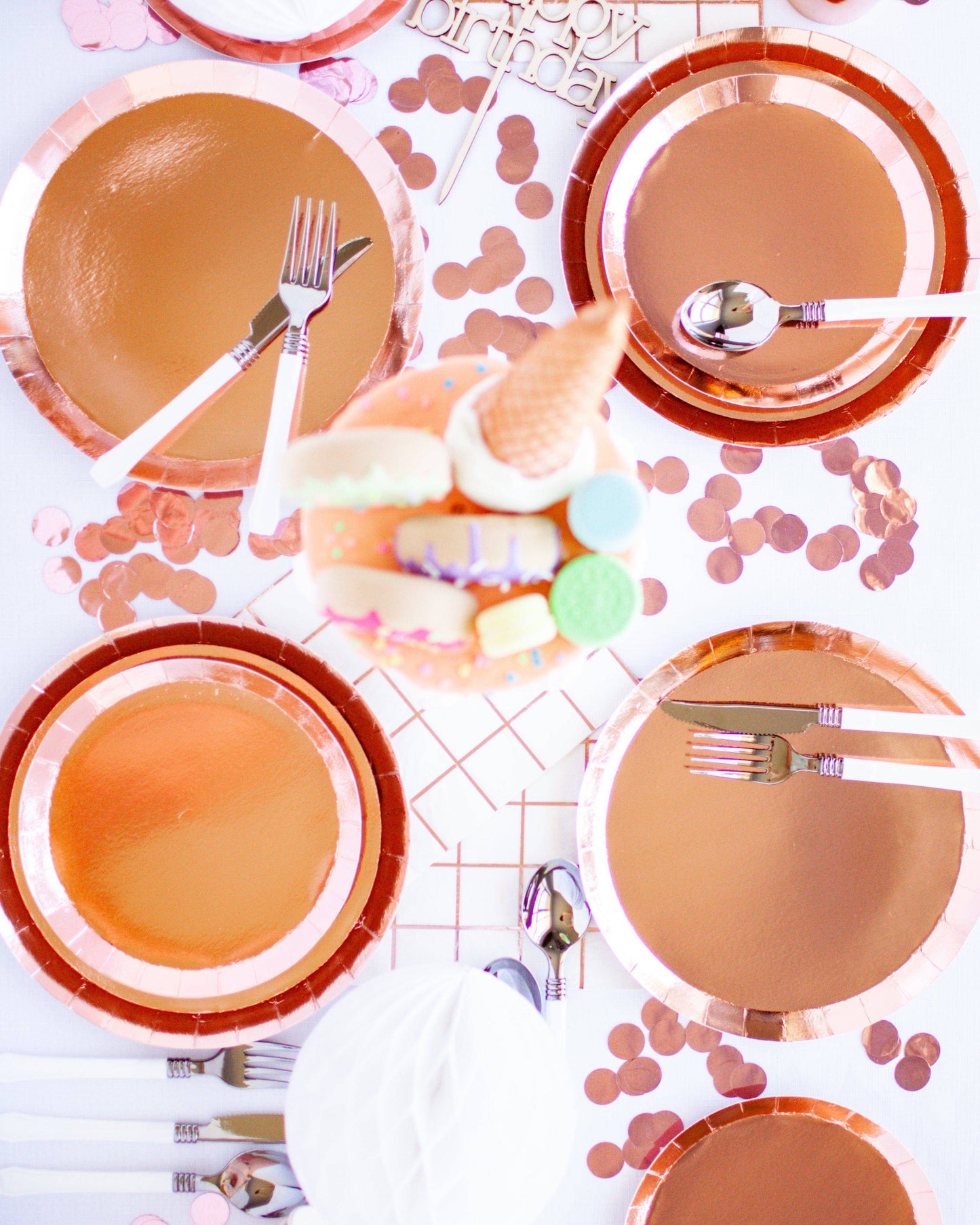 A stylish table setting featuring rose gold plates, cutlery, and colorful confetti for a festive celebration.