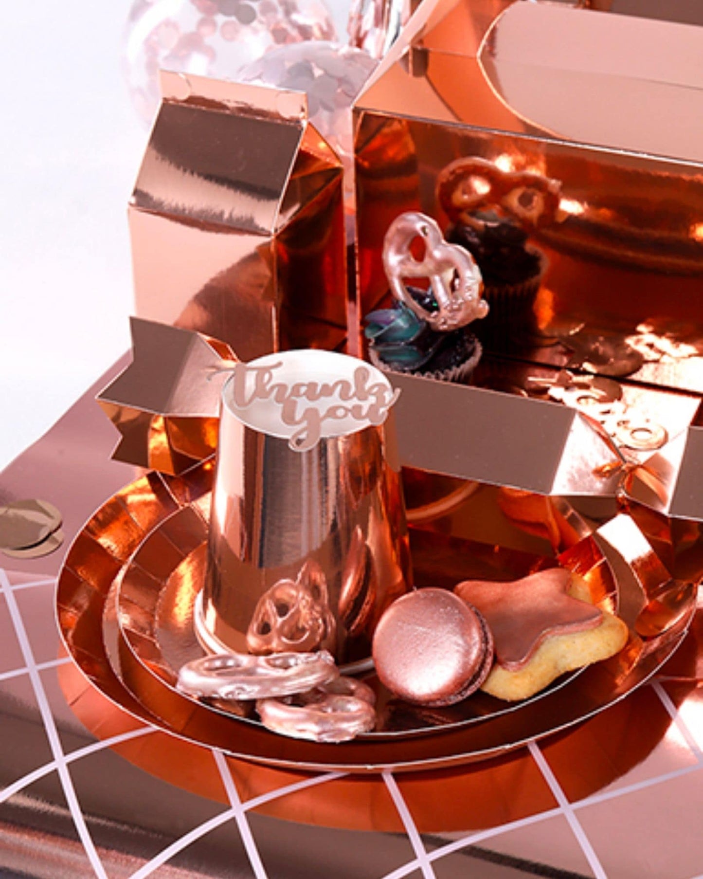 A reflective rose gold plate holds a variety of sweet treats, including cupcakes and decorative cookies.