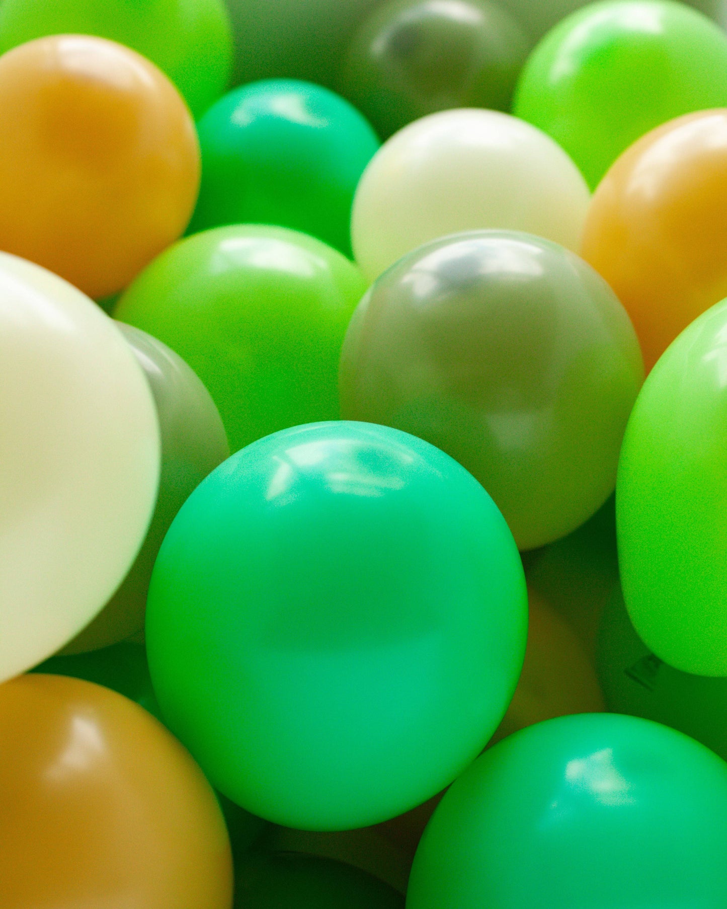 A vibrant mix of glossy green, yellow, and orange balloons clustered together, creating a festive, cheerful atmosphere.