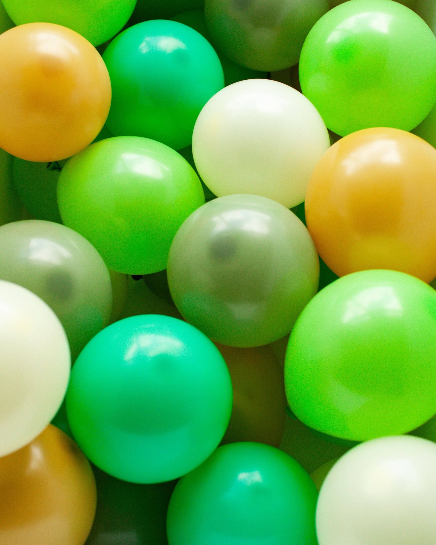 A vibrant mix of glossy, round balloons in shades of green, yellow, and white, clustered together in harmony.