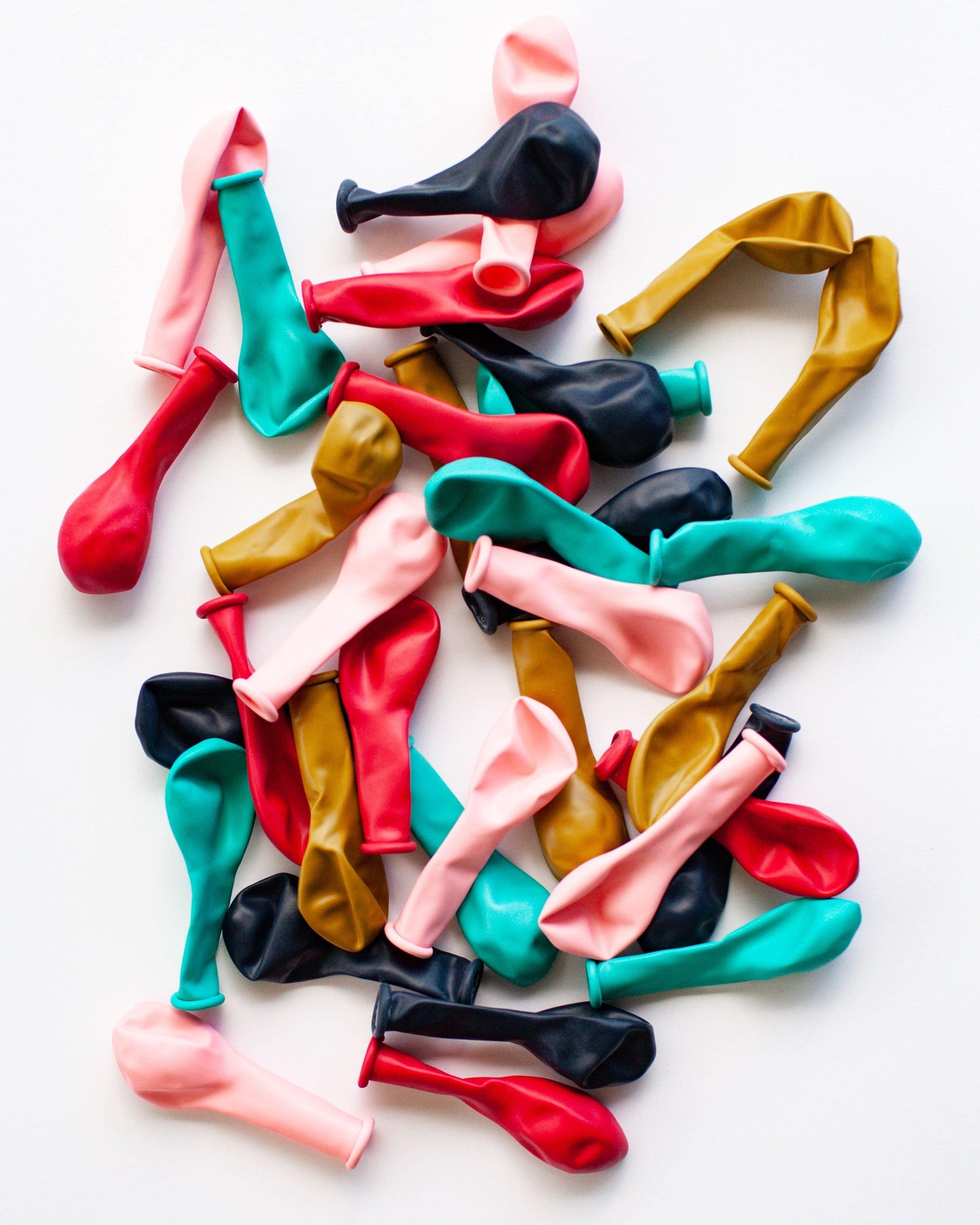 A colorful assortment of deflated balloons in shades of red, pink, teal, black, and gold on a light background.