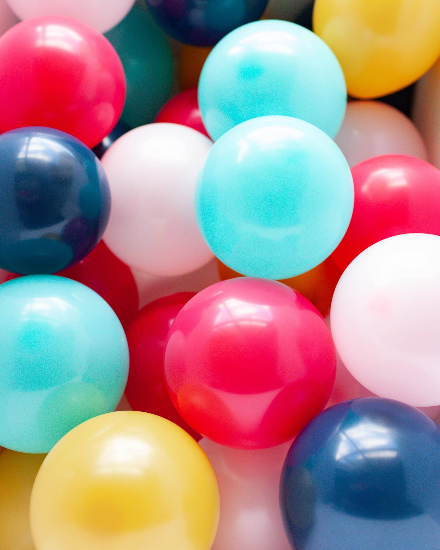 A vibrant mix of glossy balloons in shades of pink, blue, yellow, and white, clustered together in a playful arrangement.