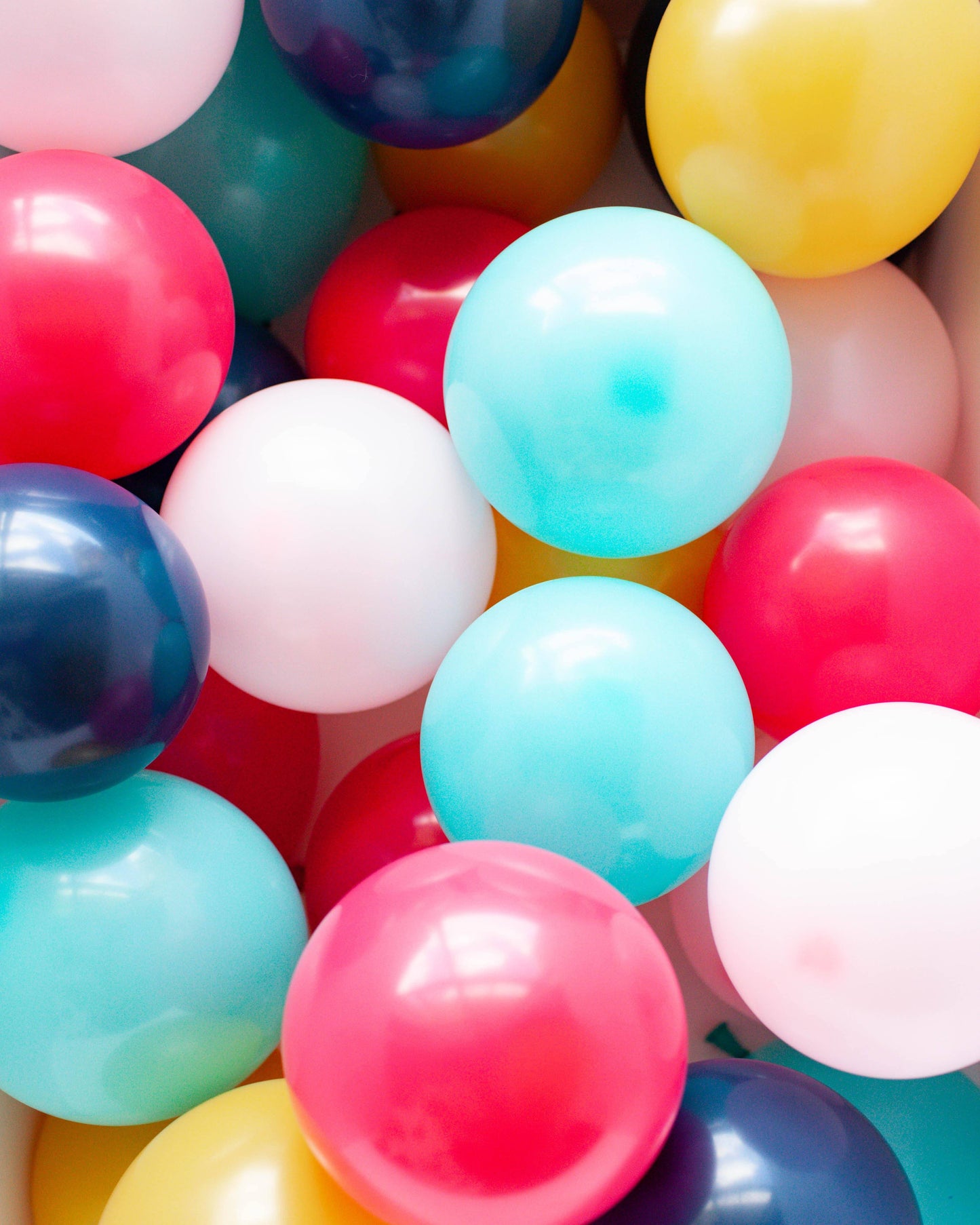 A colorful mix of glossy balloons in shades of pink, blue, yellow, and white, clustered together vibrantly.