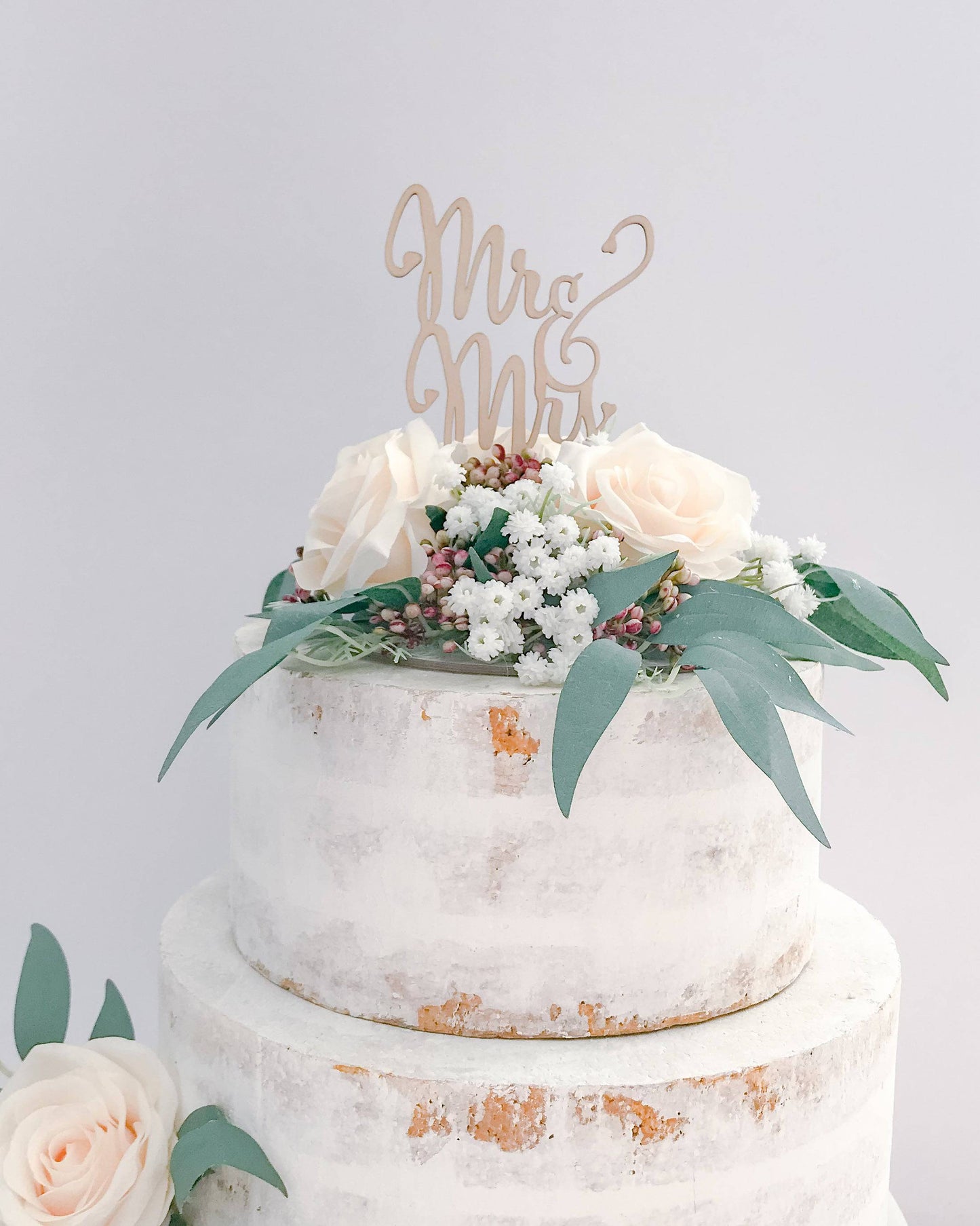 A rustic cake topped with a wooden "Mr & Mrs" sign, adorned with soft roses and greenery.