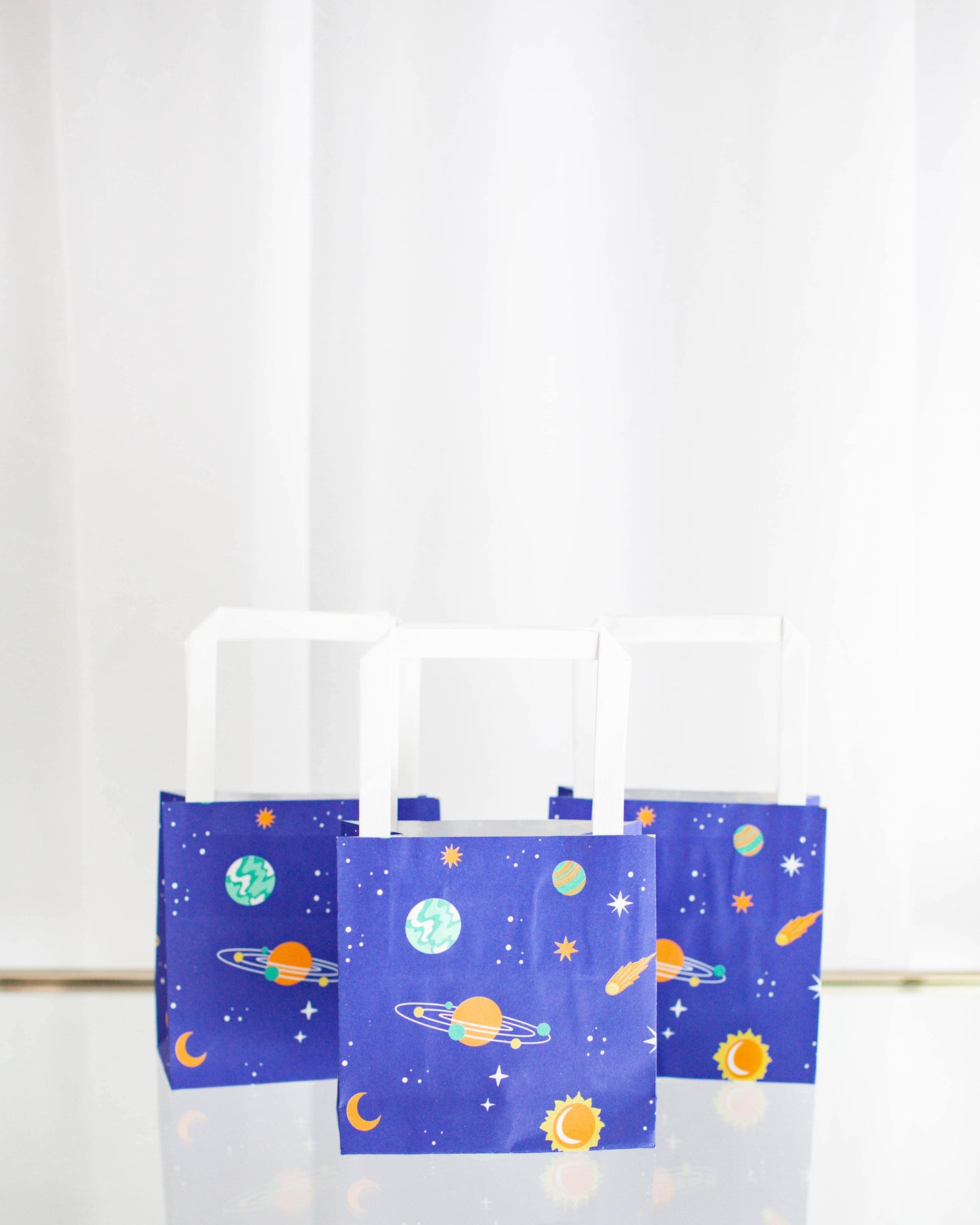 Three vibrant blue bags featuring colorful planets, stars, and celestial designs against a light background.