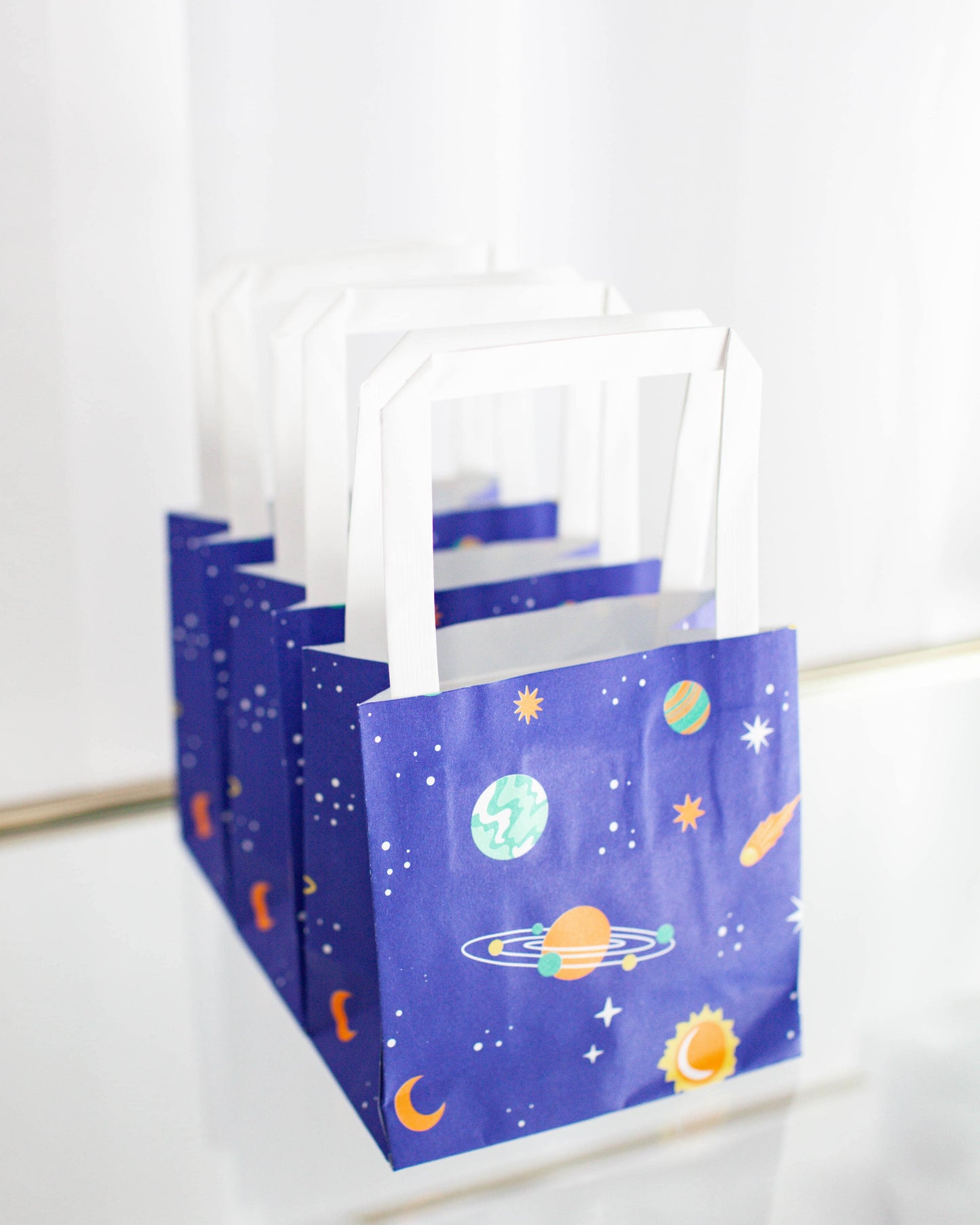A row of small bags featuring a cosmic pattern with planets, stars, and a sun on a deep blue background.
