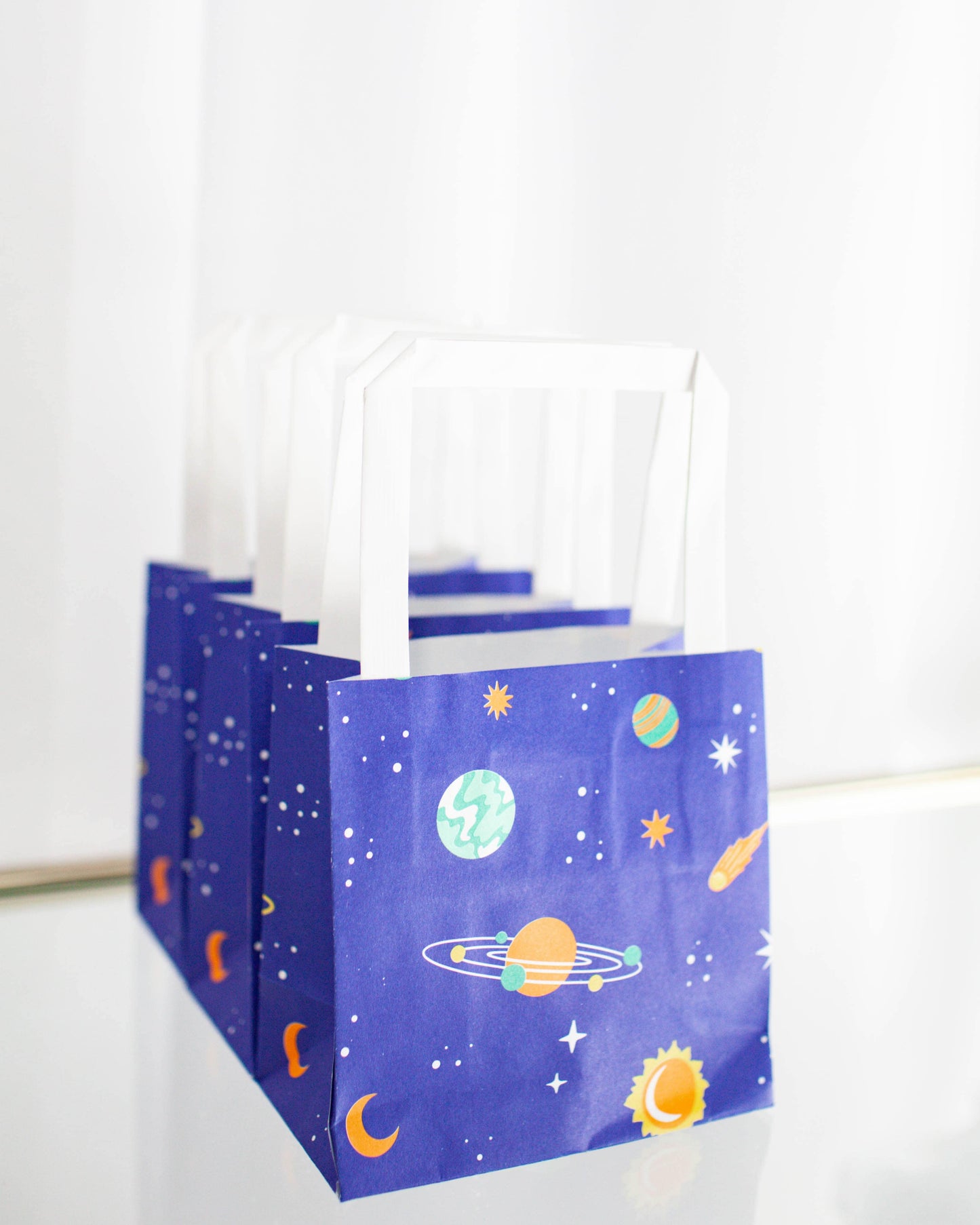Colorful bags adorned with planets, stars, and cosmic motifs against a vibrant blue background.