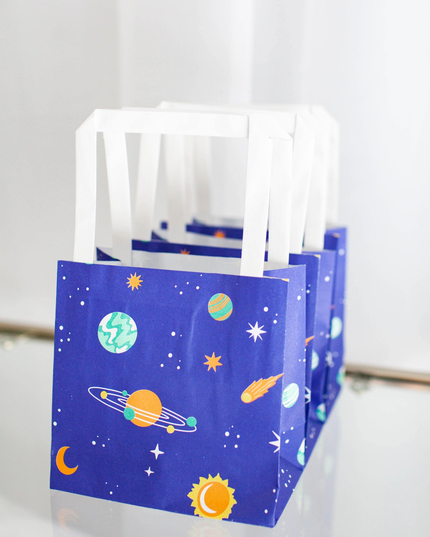 Colorful bags featuring a cosmic theme, with planets, stars, and comets against a deep blue background.