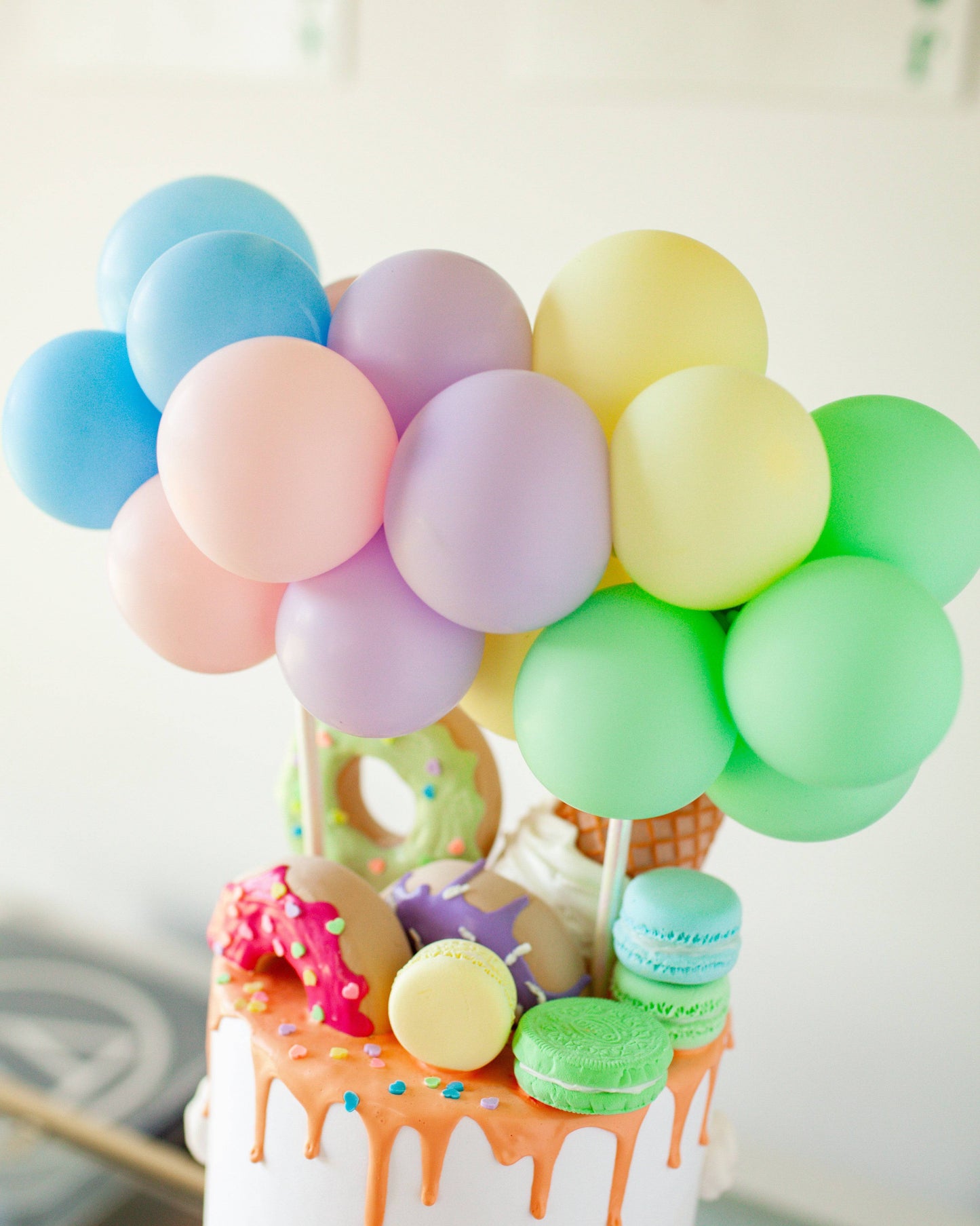 Colorful balloons in pastel shades atop a cake adorned with playful confections and vibrant sprinkles.