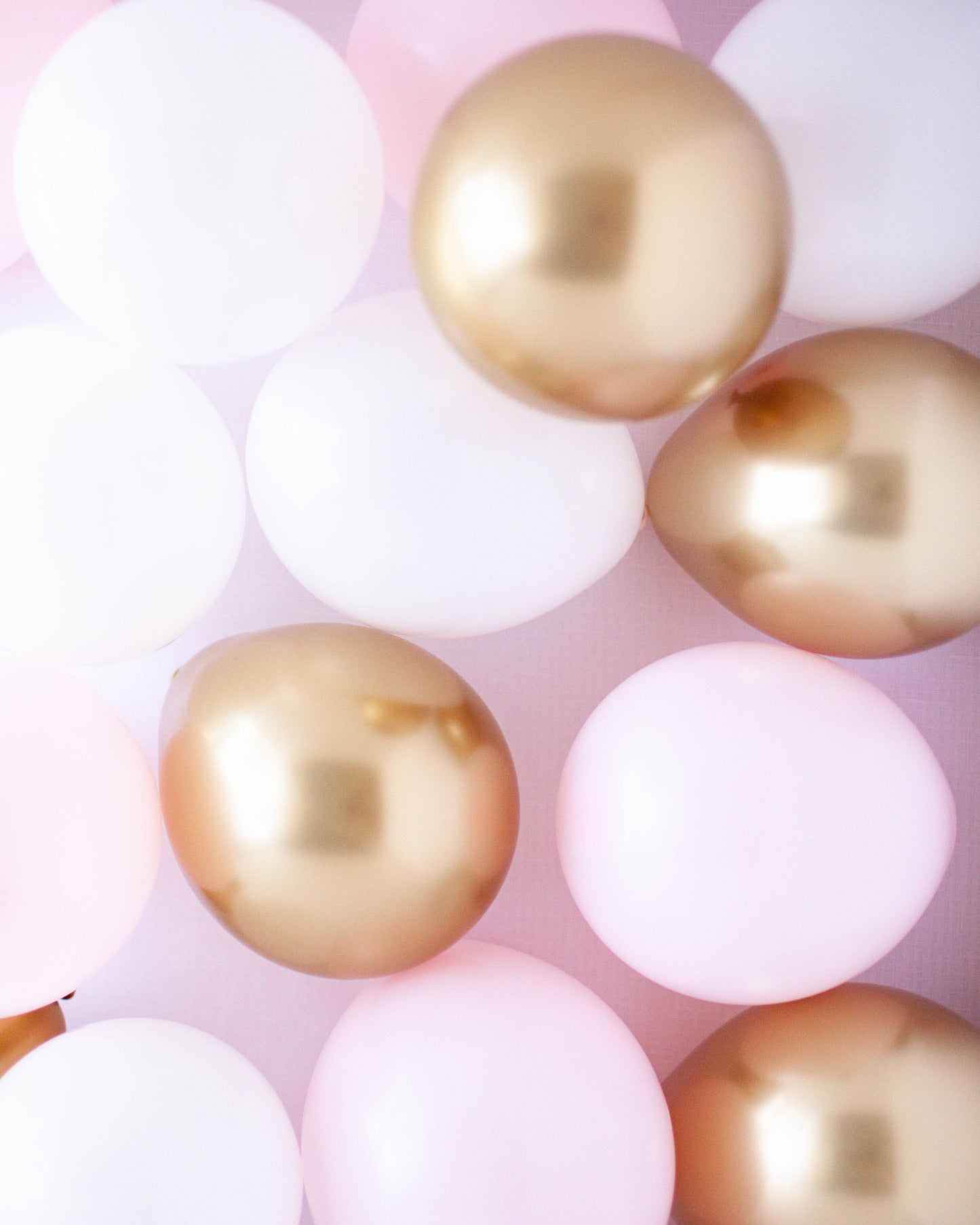 A mix of pink, white, and shiny gold balloons arranged playfully against a soft background.