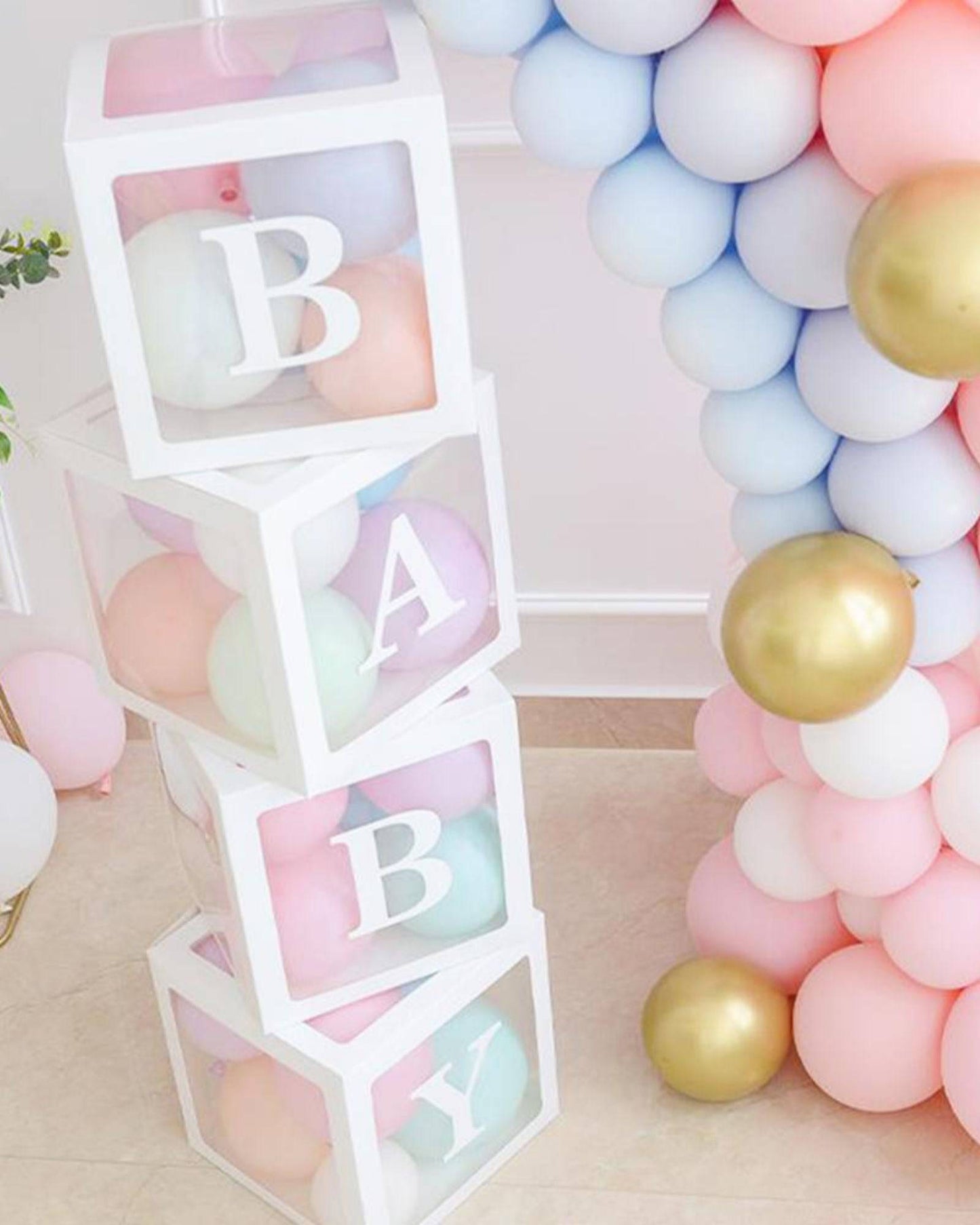 Stacked transparent boxes with pastel balloons inside spell out "BABY," surrounded by colorful balloons.