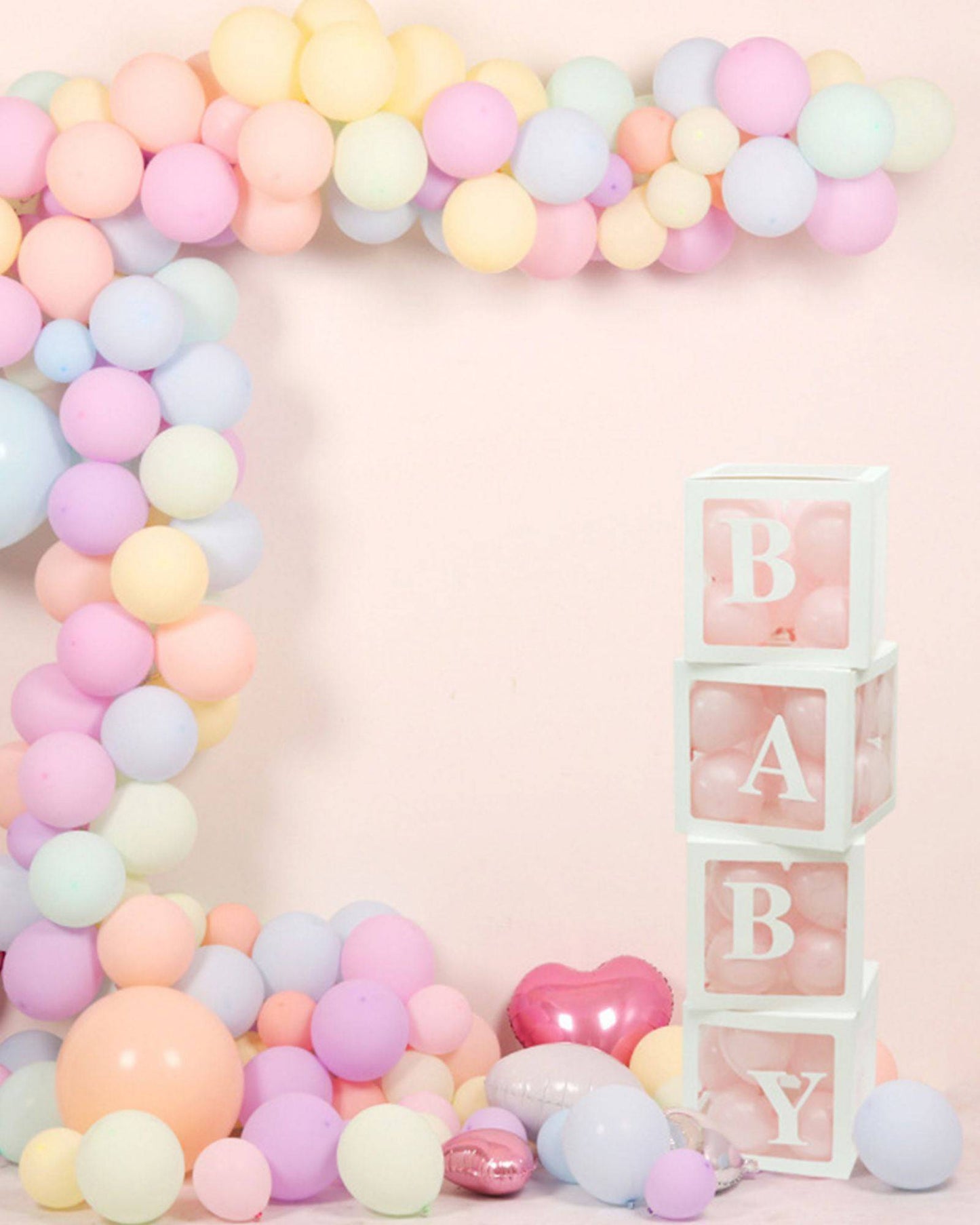Pastel balloons in soft shades surround playful white blocks spelling "BABY," with a shiny heart balloon nearby.
