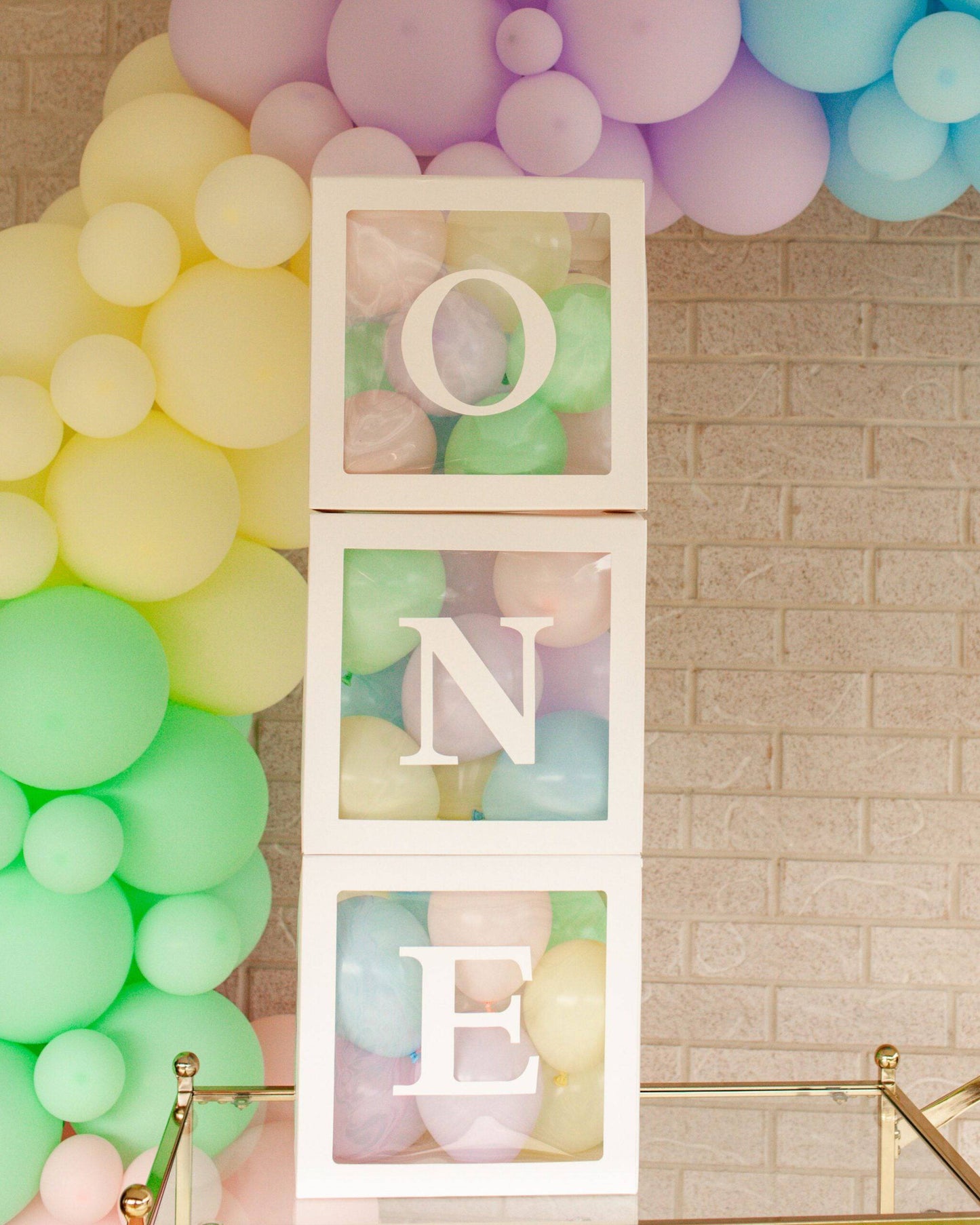Three white boxes containing colorful balloons spell out "ONE," surrounded by pastel balloons.