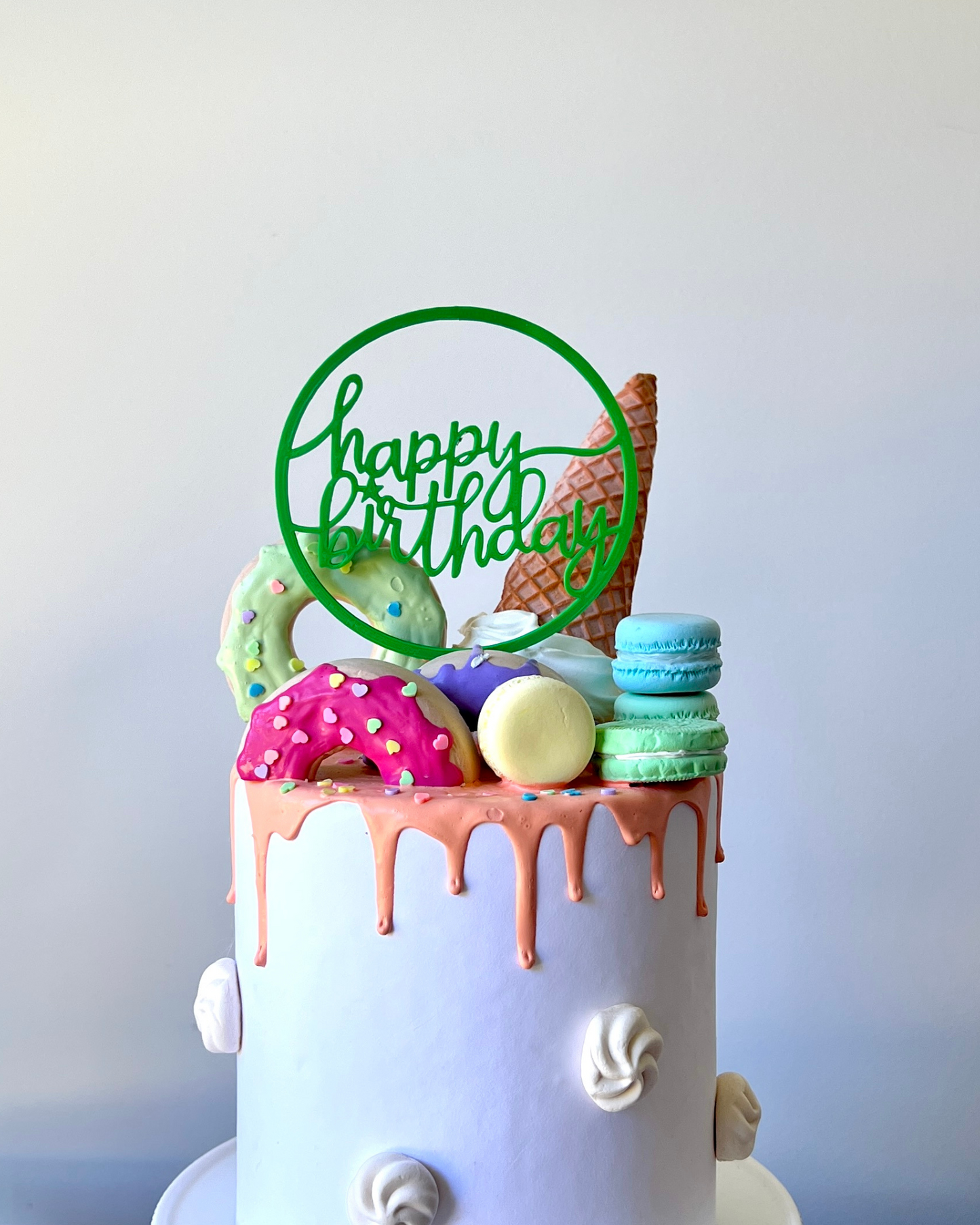 A colorful cake topped with a green "Happy Birthday" sign, ice cream cone, and various sweet treats.