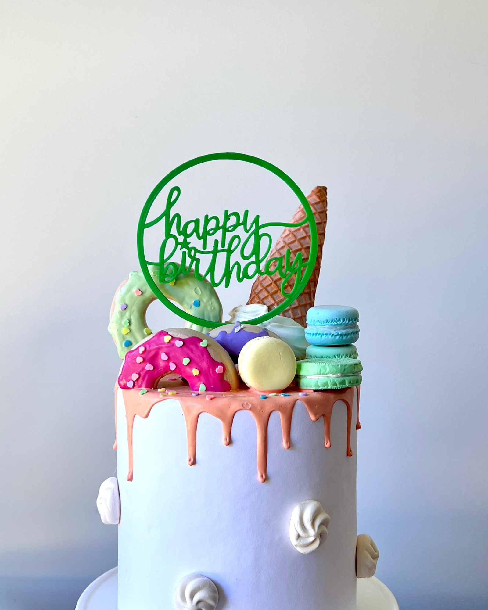 A colorful cake topped with a green "Happy Birthday" sign, ice cream cone, and various sweet treats.