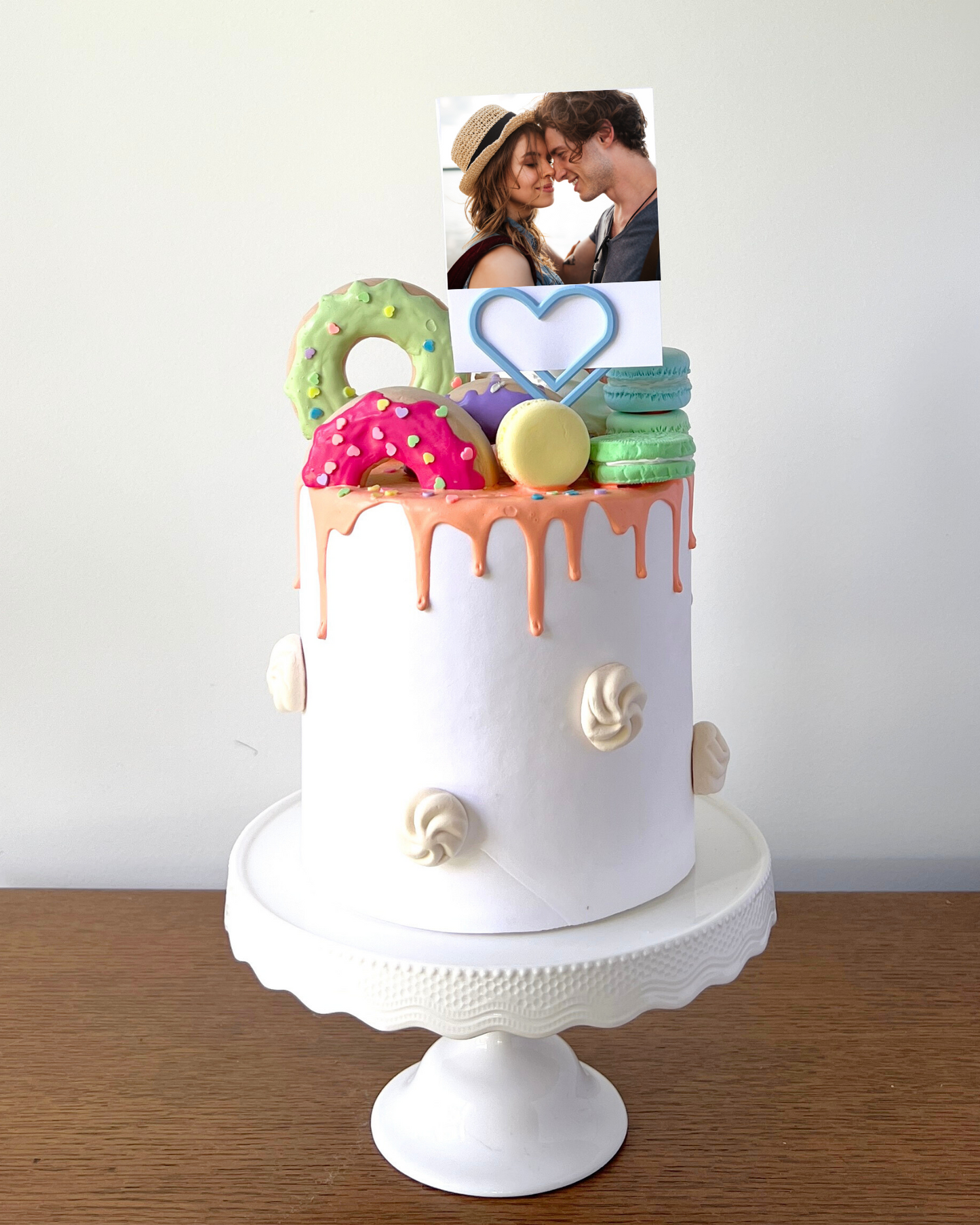 A whimsical cake topped with colorful decorations and a photo of a couple sharing a sweet moment.