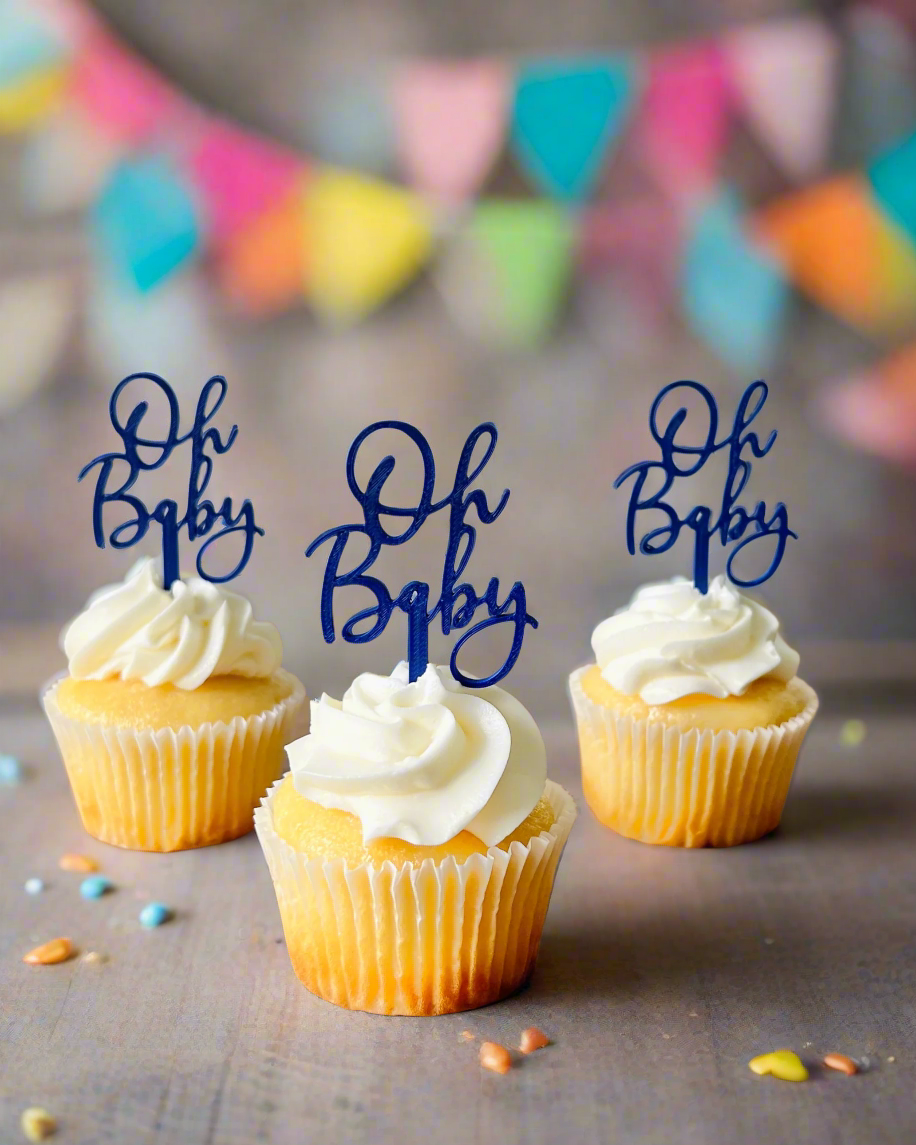 Three yellow cupcakes topped with white frosting and blue "Oh Baby" toppers, surrounded by colorful confetti and bunting.