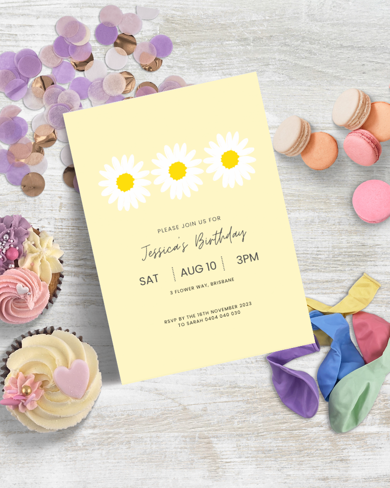 A bright birthday invitation surrounded by colorful macarons, cupcakes, confetti, and balloons on a wooden surface.