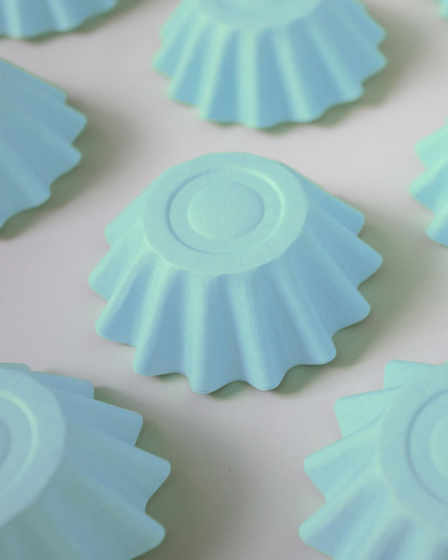 Light blue, fluted shapes arranged closely, featuring a smooth, circular top and a soft matte finish.