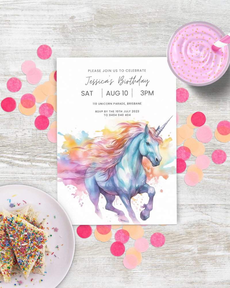 Colorful unicorn illustration with birthday invitation, sprinkles, and confetti on a light wooden surface.