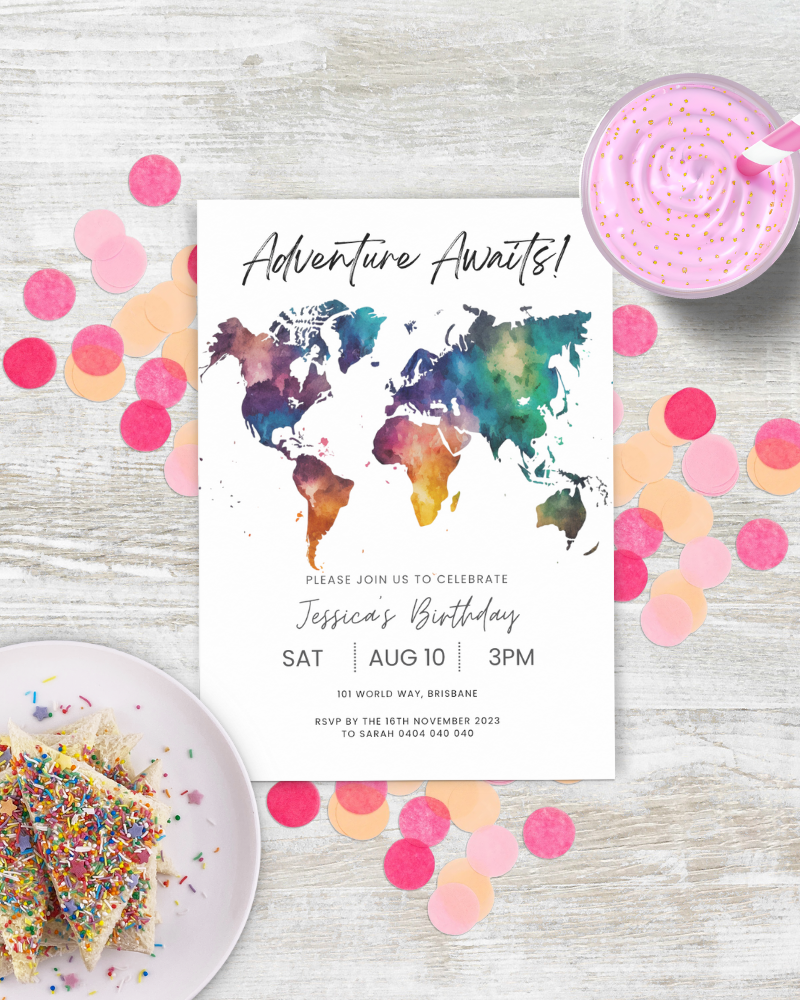 Colorful world map invitation on a wooden surface, surrounded by confetti and a pink dessert with sprinkles.