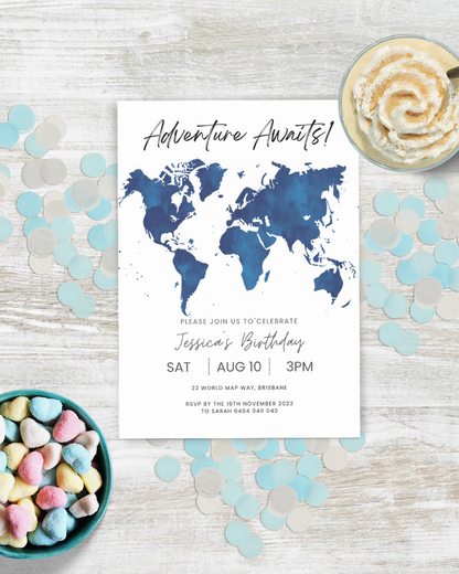 A birthday invitation featuring a blue world map and colorful heart-shaped candies on a light wooden surface.