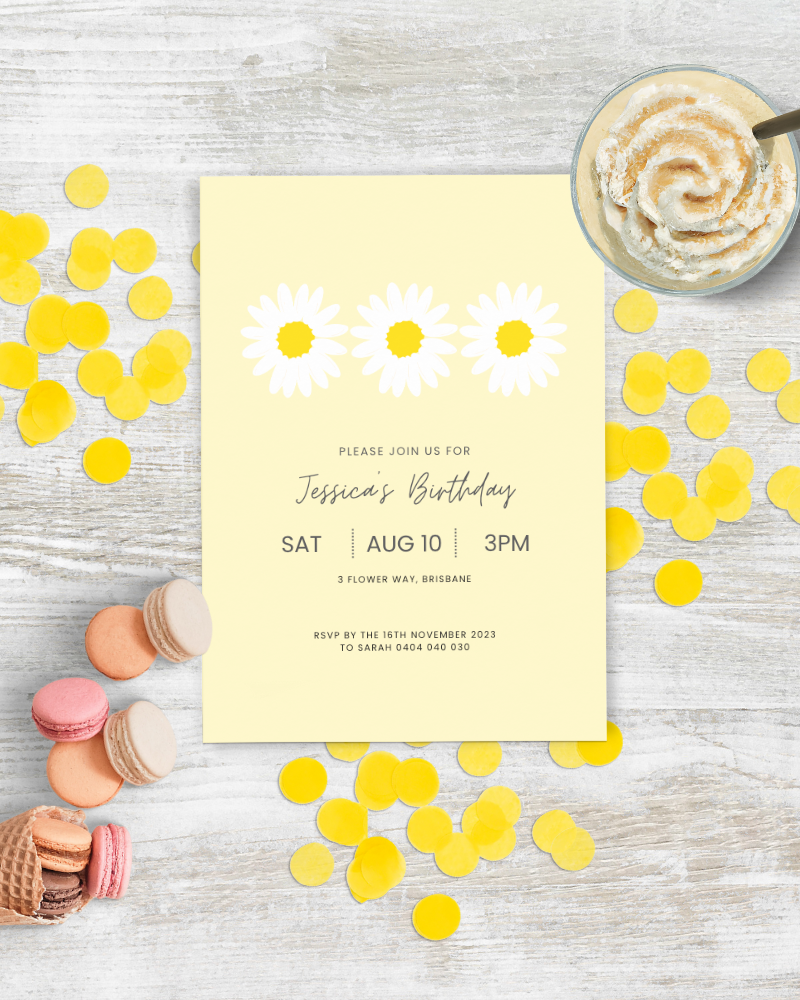 A cheerful birthday invitation with yellow daisies, surrounded by colorful confetti and sweet treats on a wooden surface.