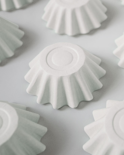 A close-up of white, fluted shapes with a smooth center, arranged on a soft gray background.
