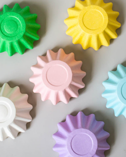 Colorful, textured shapes in green, yellow, pink, blue, white, and purple arranged on a light gray surface.