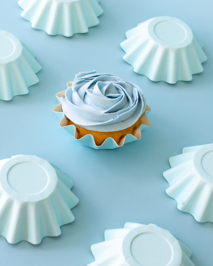 A light blue frosted dessert with a rose design, surrounded by pastel blue cup shapes on a soft blue background.