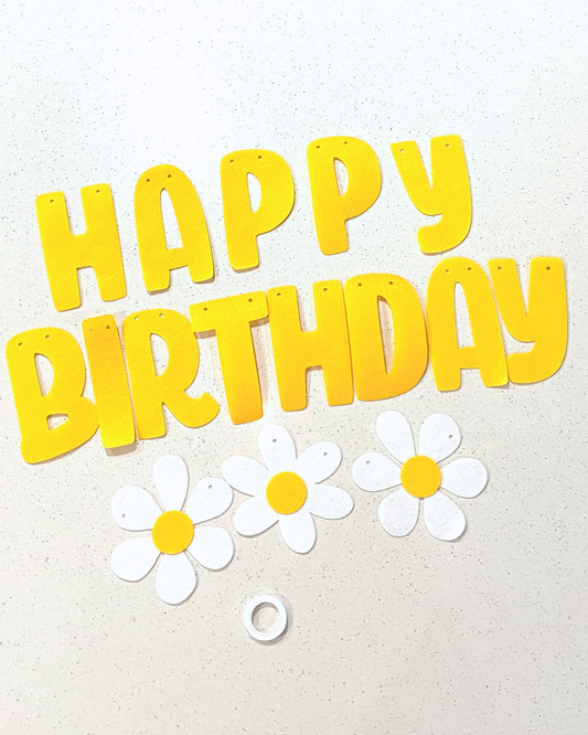 Bright yellow letters spell "HAPPY BIRTHDAY" alongside white flowers with yellow centers on a light surface.