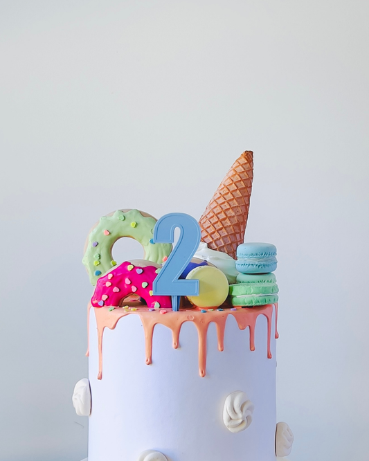 A whimsical celebration centerpiece featuring colorful treats, a number two, and a playful, dripping frosting effect.