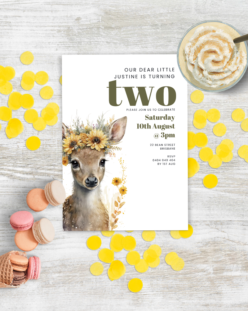 A whimsical invitation featuring a fawn adorned with flowers, surrounded by colorful confetti and treats.