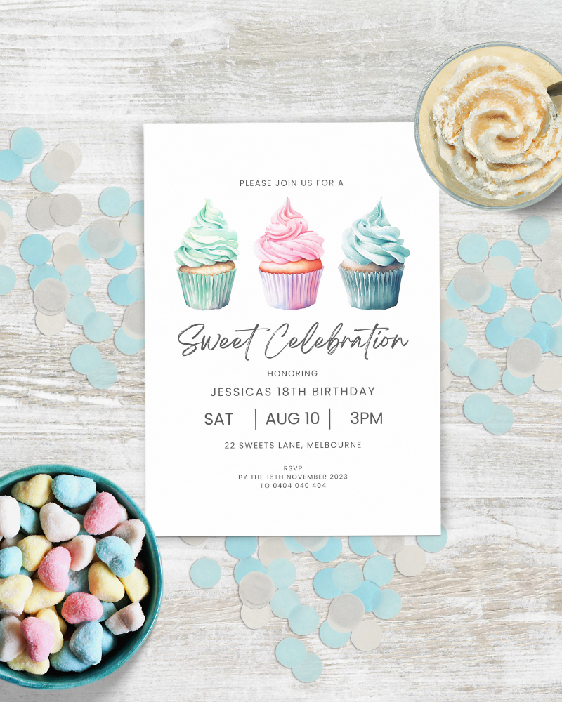 Colorful cupcakes on a celebration invitation surrounded by pastel confetti and heart-shaped candies on a wooden surface.