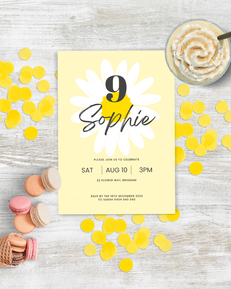 A cheerful birthday invitation featuring a daisy design, colorful confetti, and macarons on a rustic wooden surface.