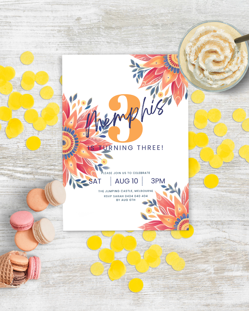 Colorful invitation featuring floral accents, yellow confetti, and macarons on a rustic wooden table.